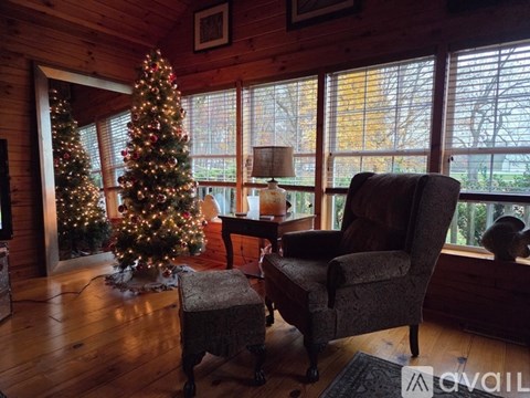 A Christmas tree stands in a living room with a chair and ottoman.