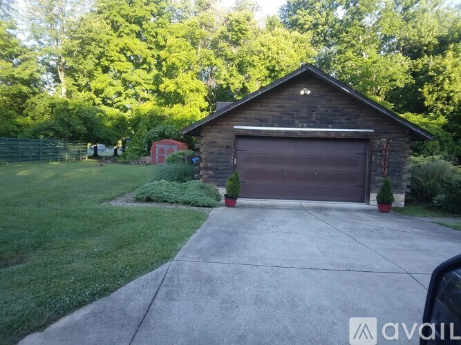 A wooden garage with a brown door is surrounded by greenery.