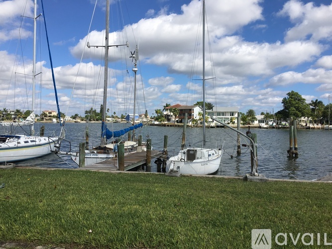 A sailboat is docked at a marina with other boats and buildings in the background.