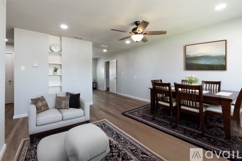 A living room with a white couch, a wooden dining table with chairs, and a ceiling fan.