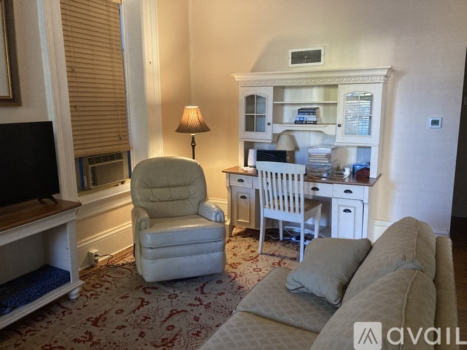 A living room with a grey sofa, a white chair and a white cabinet with a microwave.