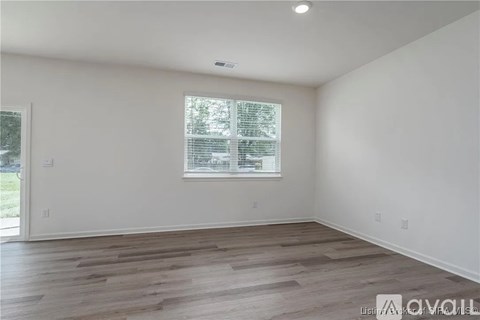 A spacious room with wooden flooring and a window with blinds.