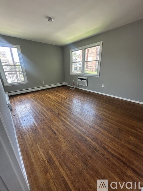 A room with wooden flooring and two windows.