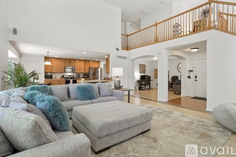 A living room with a grey couch and a grey ottoman with a blue pillow on it.