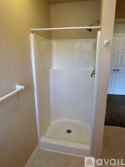 A white shower stall with a door and a drain.