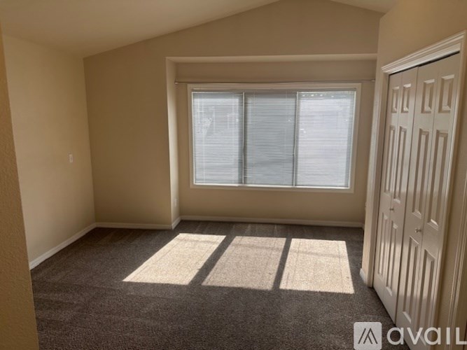 A room with a carpeted floor, a window with blinds, and a door.