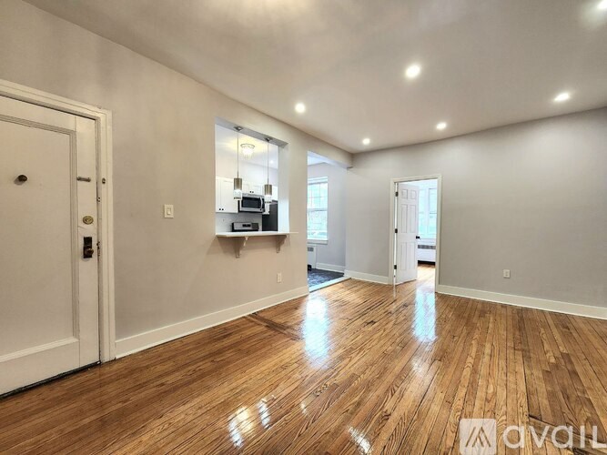 A room with wooden floors and white walls, with a door on the left and a window on the right.