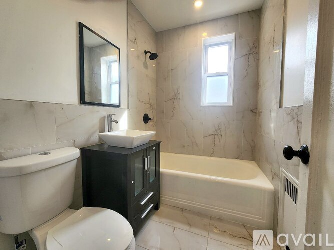 A bathroom with a white toilet, a white sink, a black cabinet, and a white bathtub.