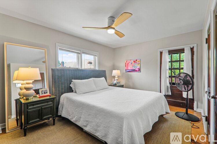 A bedroom with a bed, a fan, and a dresser with a lamp on it.