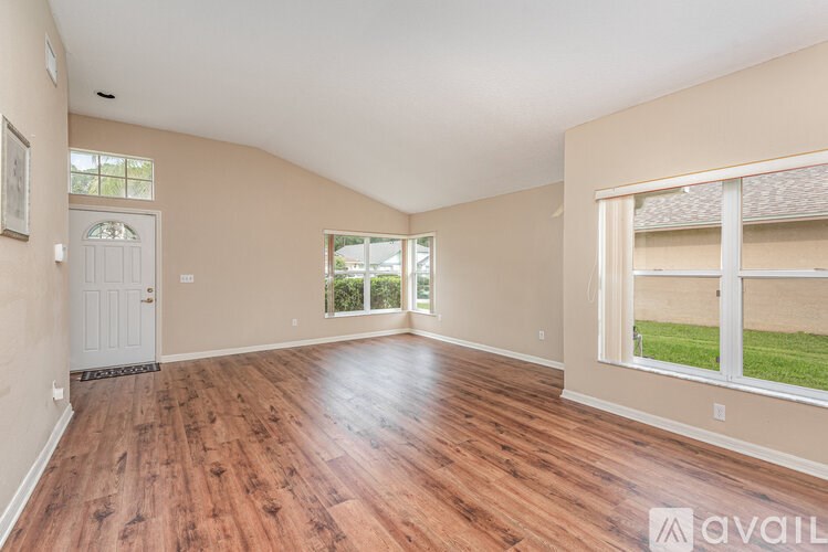 A room with wooden flooring and a large window overlooking a grassy area.