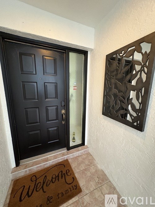 A black door with a glass window and a mat on the floor that says "Welcome".