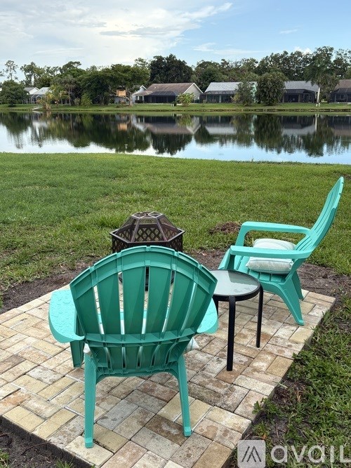 Two green chairs and a table are on a patio by a lake.