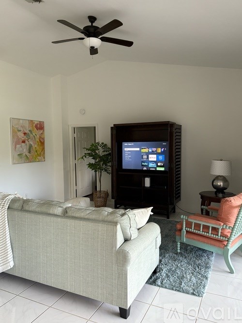 A living room with a couch, a television, and a fan.