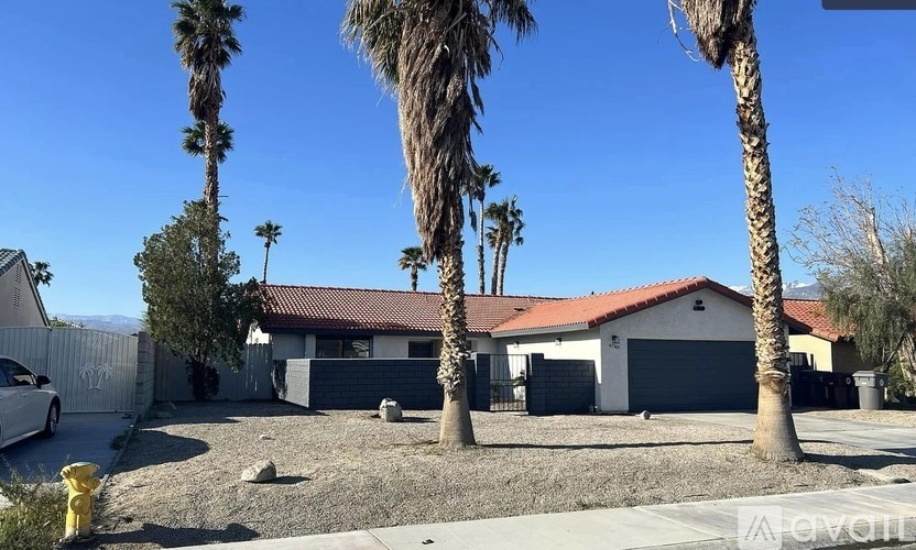 A house with a red roof and a white garage door is surrounded by palm trees.