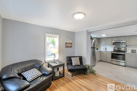 A living room with a black leather couch and a kitchen area with stainless steel appliances.