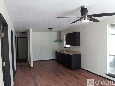 A room with a ceiling fan and a kitchenette.