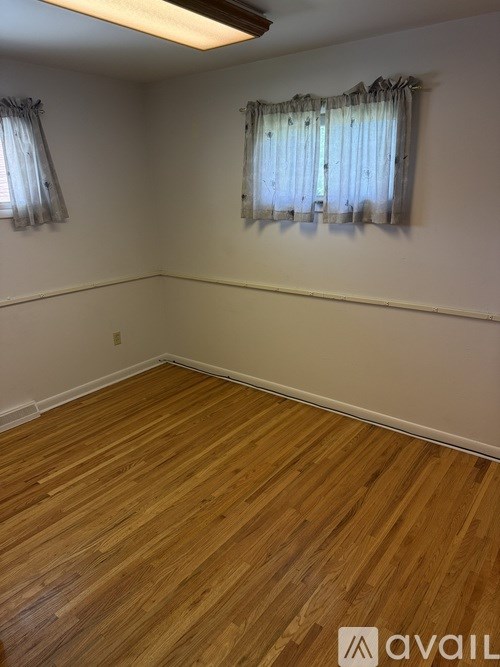 A room with wooden flooring and two windows with curtains.