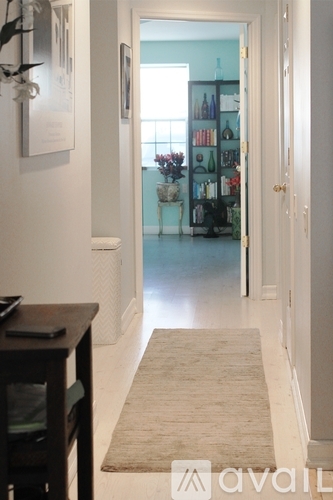A hallway with a rug and a doorway leading to a room with a shelf.