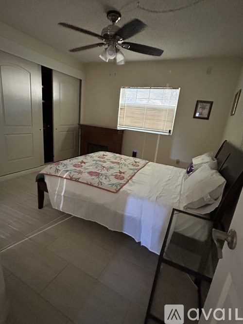 A bedroom with a bed, a ceiling fan, and a window with blinds.