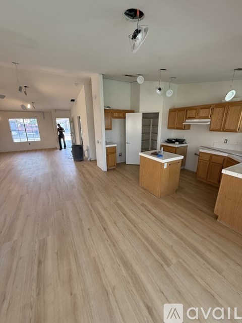 A large empty room with wooden floors and a kitchen area in the background.