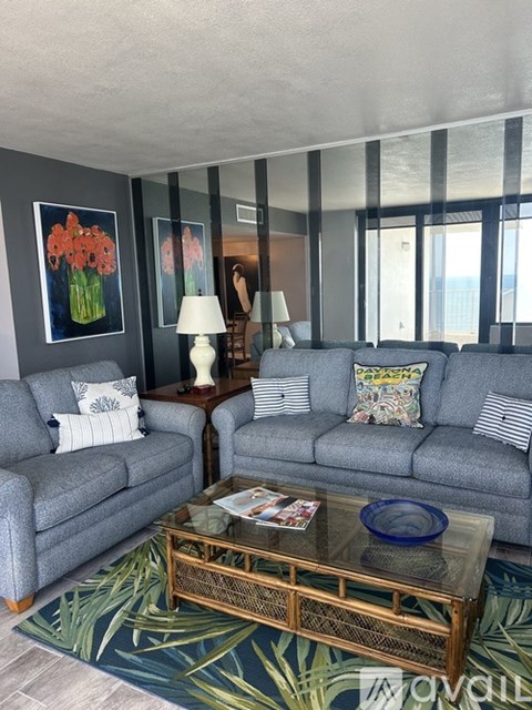 A living room with two grey couches, a glass coffee table, and a painting of flowers on the wall.