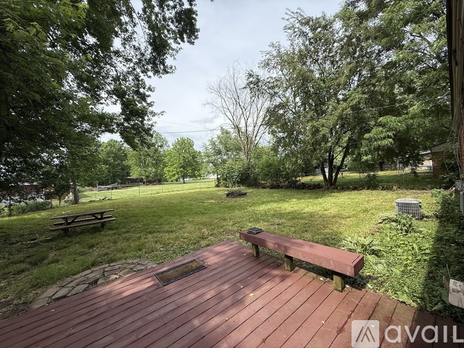 A wooden deck with a bench in the middle of a grassy area surrounded by trees.