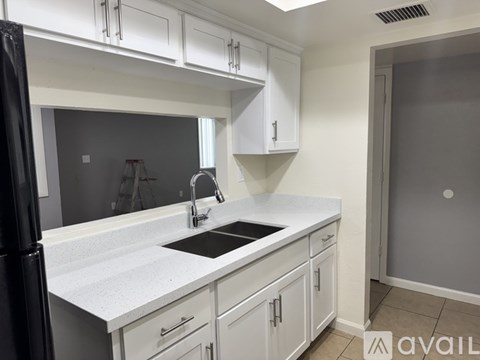 A kitchen with white cabinets and a black fridge.