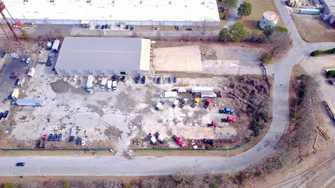 A large open field with a few cars and people scattered around.