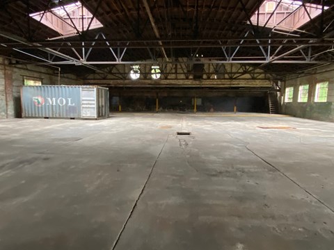 A large empty warehouse with a container labeled "MOL" in the corner.