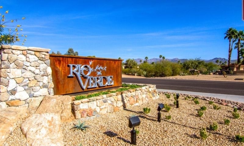 A sign that says Rio Verde in front of a stone wall.