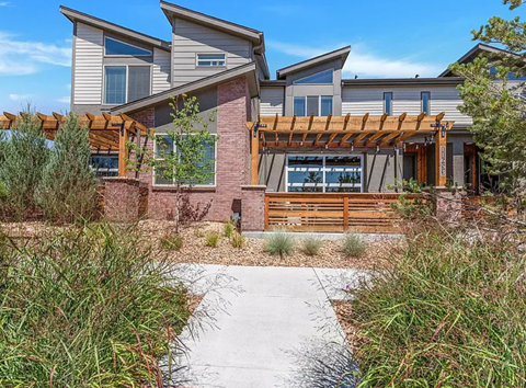 A modern house with a wooden pergola and a concrete pathway leading to the entrance.