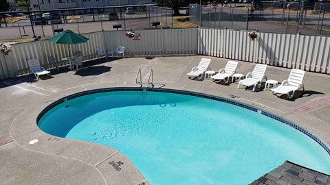 A swimming pool surrounded by a metal fence and lounge chairs.
