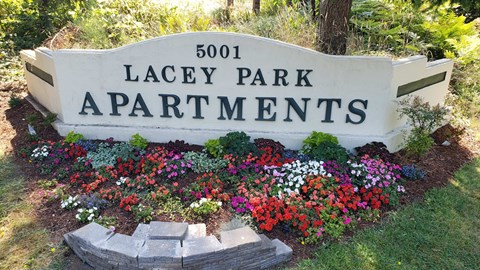 A sign for Lacey Park Apartments is surrounded by flowers.