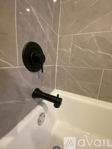 A black faucet is turned on in a white bathtub.