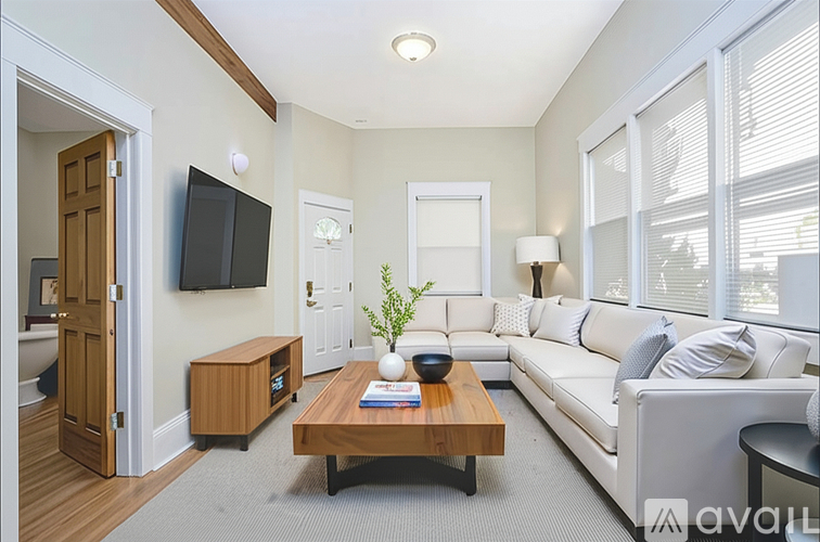 A modern living room with a white sofa, wooden coffee table, and a flat-screen TV mounted on the wall.