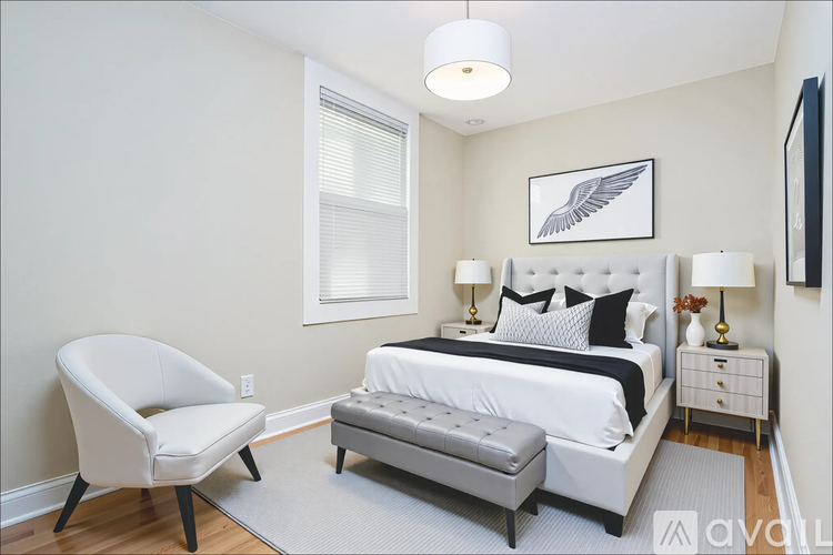 A white chair sits in a bedroom with a bed and nightstand.
