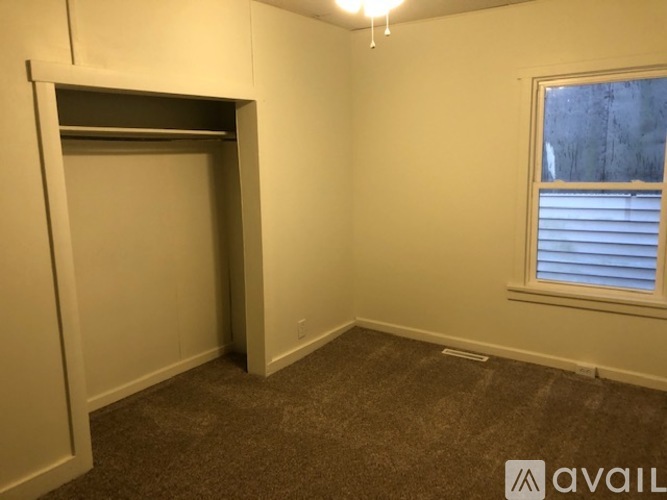 A room with a carpeted floor, a window with blinds, and a doorway leading to another room.