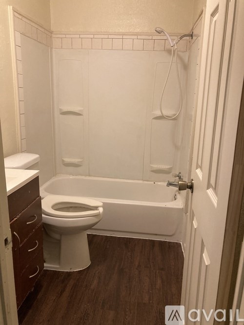 A white bathroom with a toilet, tub, and wooden floors.