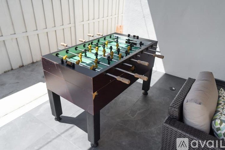 A foosball table is on a patio with a couch and pillow behind it.