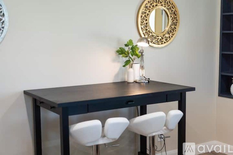 A black dining table with four white chairs and a mirror above it.