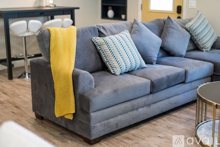 A grey couch with a yellow throw and blue pillows.