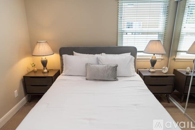 A bedroom with a large bed, two nightstands with lamps, and a window with blinds.