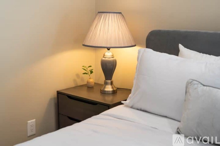 A bedroom with a bed, a nightstand with a lamp and a plant on it.