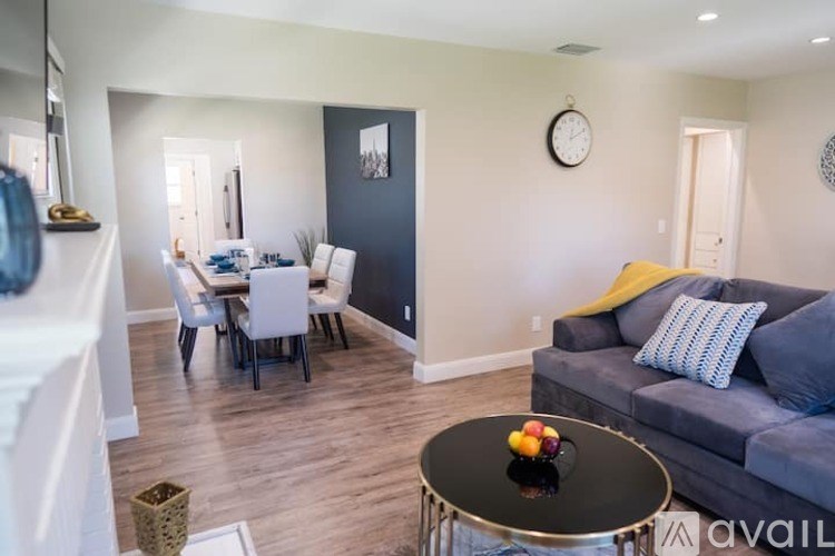 A living room with a grey couch and a dining table with chairs.