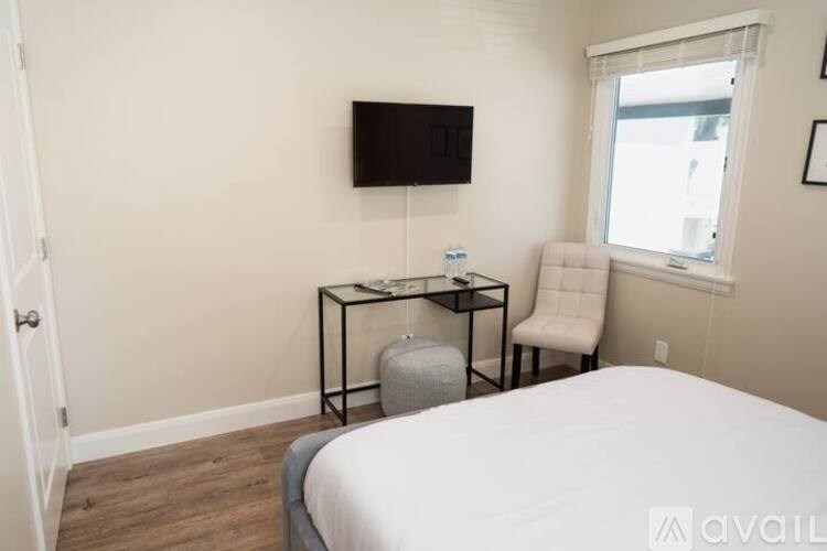 A bedroom with a bed, chair, and a small table with a television mounted on the wall.