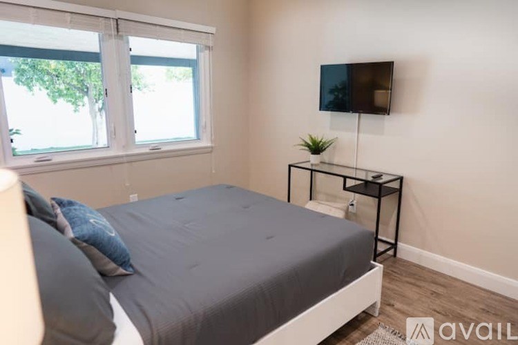 A bedroom with a bed, a small table with a plant, and a flat-screen TV mounted on the wall.