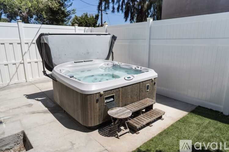 A hot tub is surrounded by a white fence and has a wooden deck.