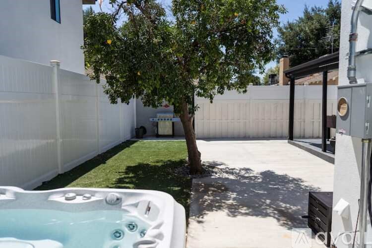 A hot tub sits in a backyard with a tree and a fence.