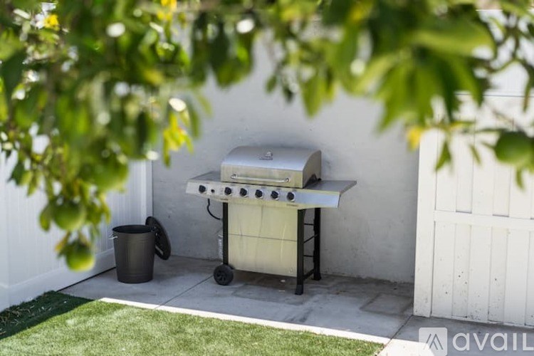 A barbecue grill is set up on a patio with a trash can nearby.