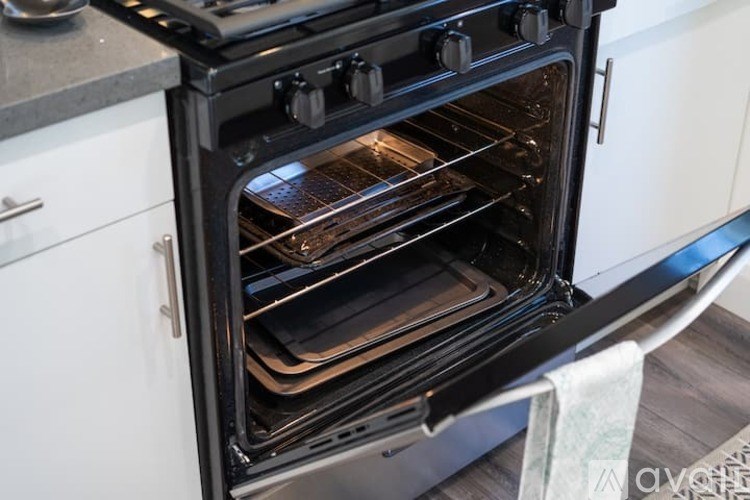 A modern black oven with four burners is open, showing two pans baking inside.